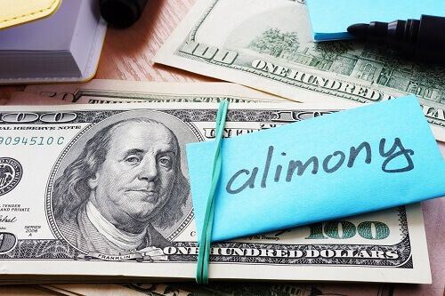 Stack of hundred dollar bills and a note with the word "alimony" on it tied together with a rubber band.