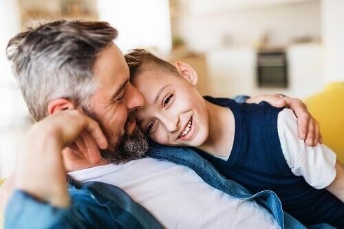 Smiling father sits with his arm around his smiling son.
